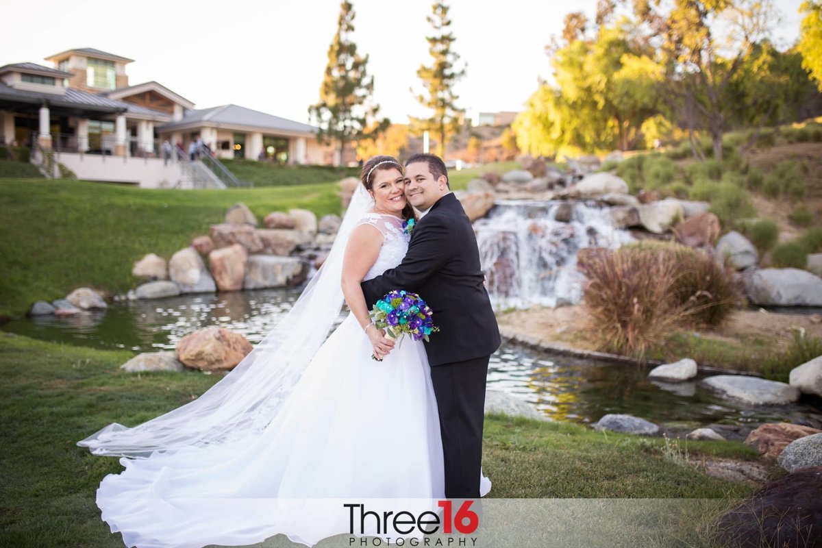 Bride and Groom embrace for a photo next to small waterfall