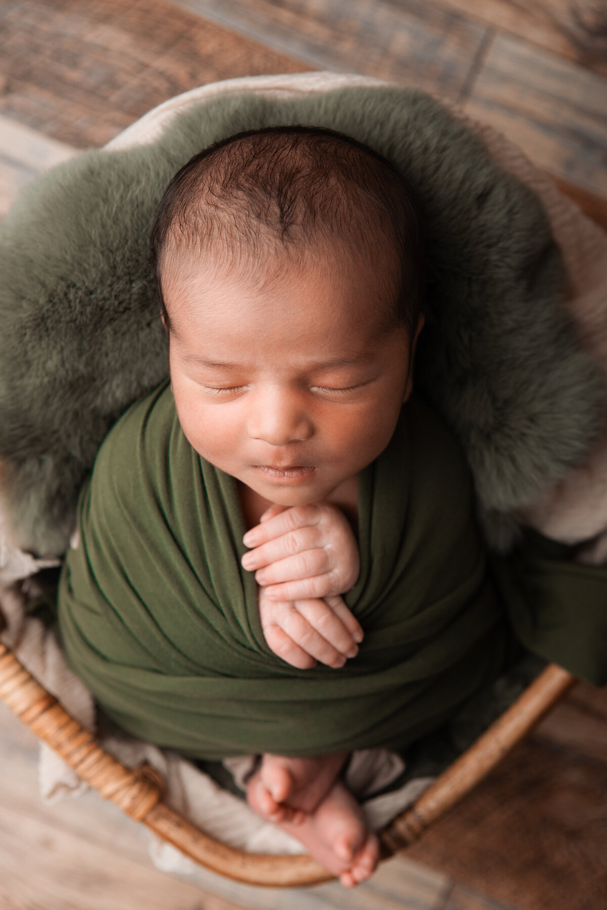 Olive green wrapped newborn pose in a bamboo basket