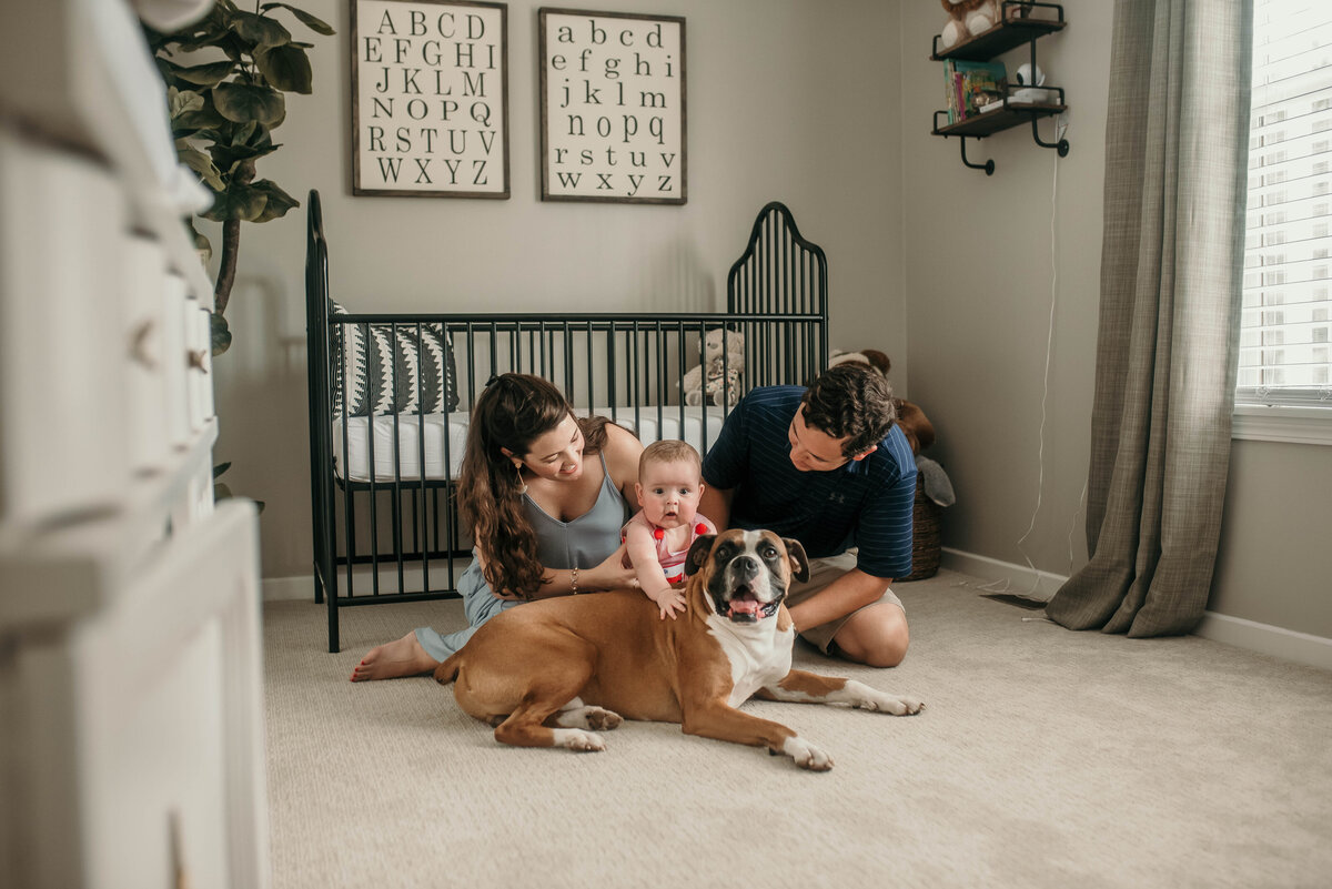Mom, dad, baby, and dog sit in front of crib