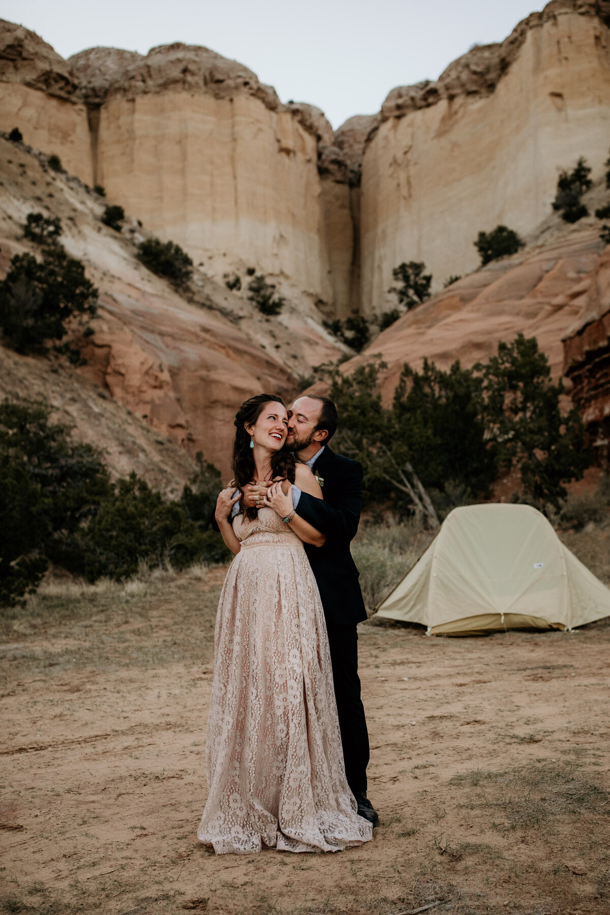 groom kissing bride at campsite in front of a desert canyon