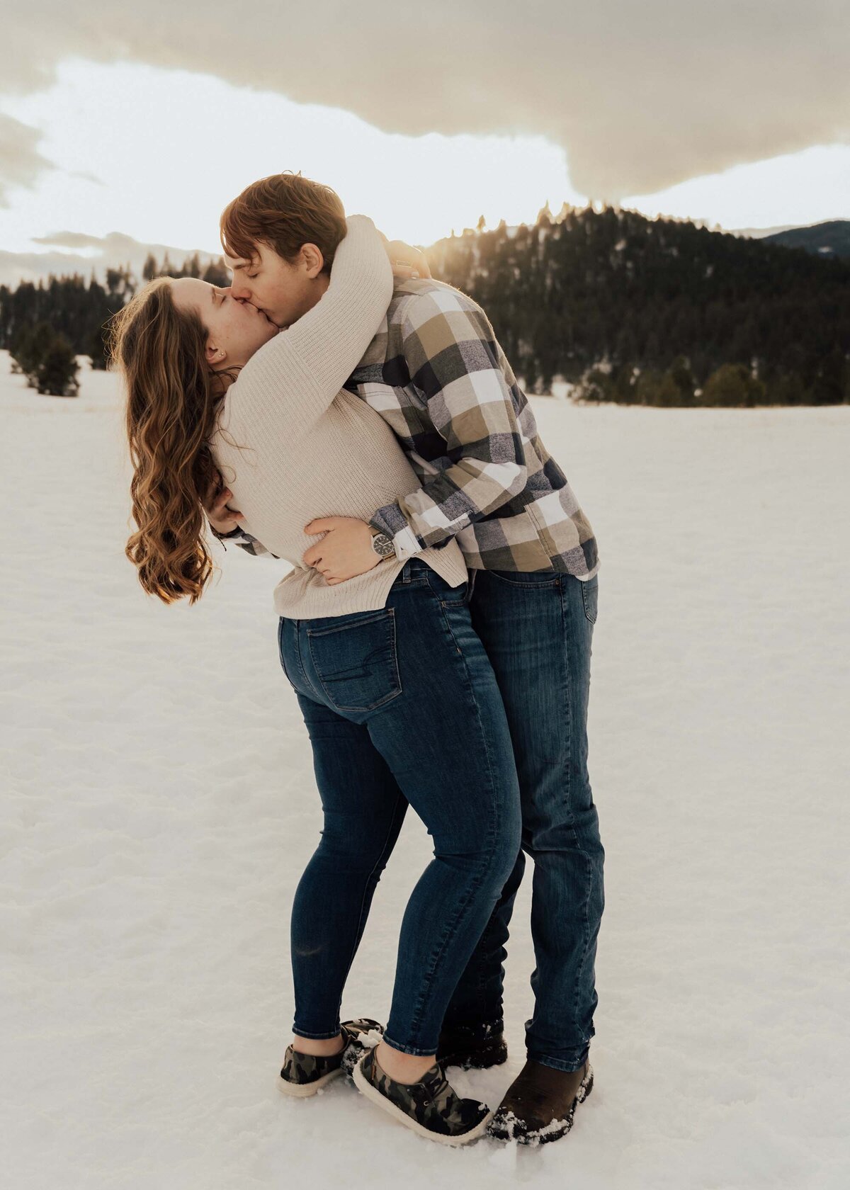 Maddie Rae Photography couple dip kissing. the sun is shining from behind the mountains, its snowy out