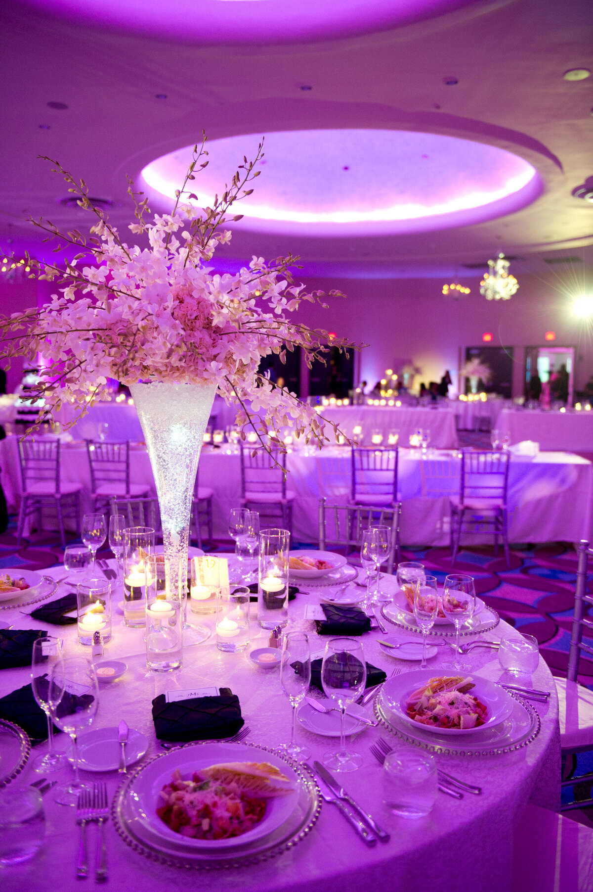 Elegant wedding reception in a hall with dinner tables, chairs and  floral centerpieces in purple theme