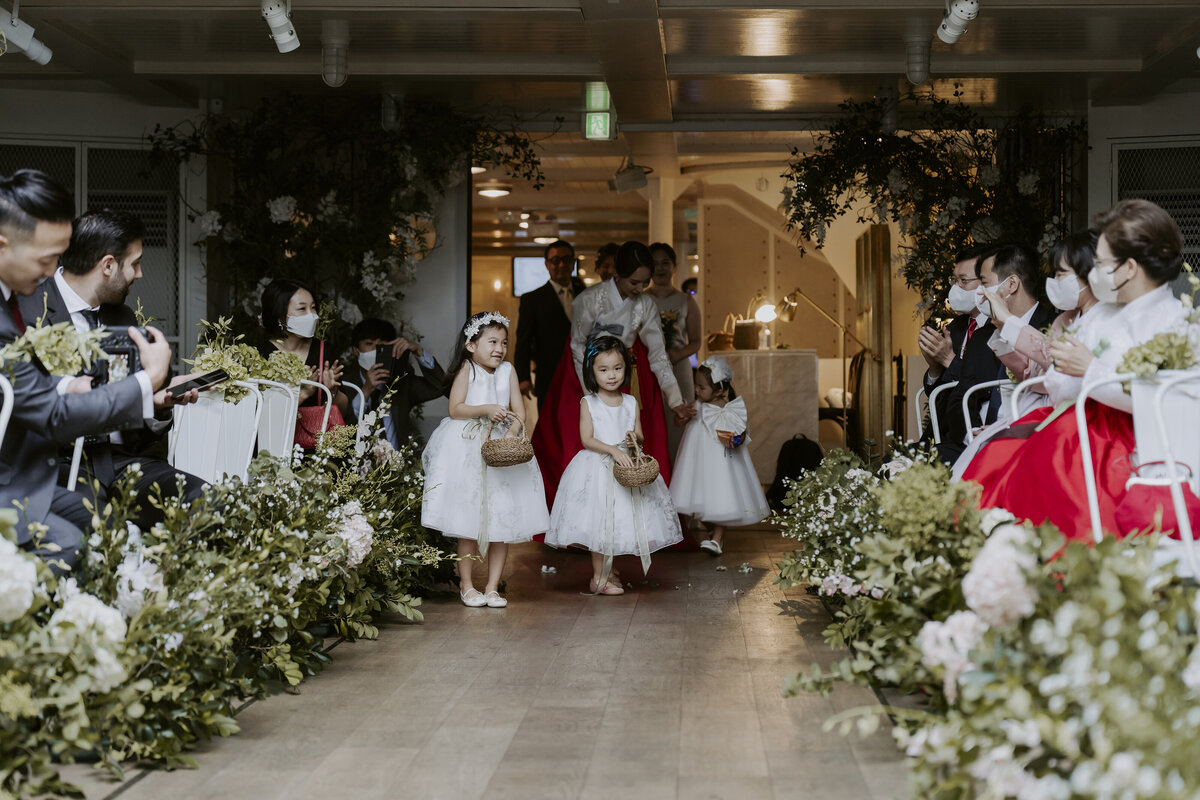 little flower girls walking down the aisle while wearing their little white dress