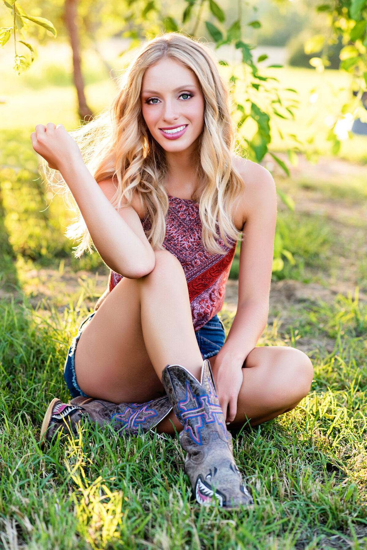 King William high school senior girl casually poses under tree wearing bandana top and cowboy boots for senior pictures.