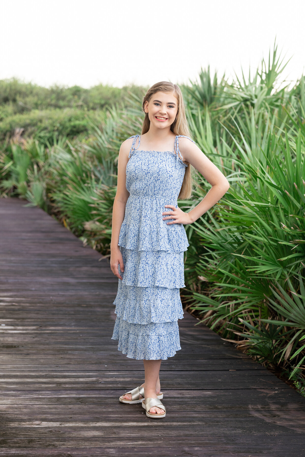 A young girl smiling with one hand on her hip, on a boardwalk in Rosemary Beach.