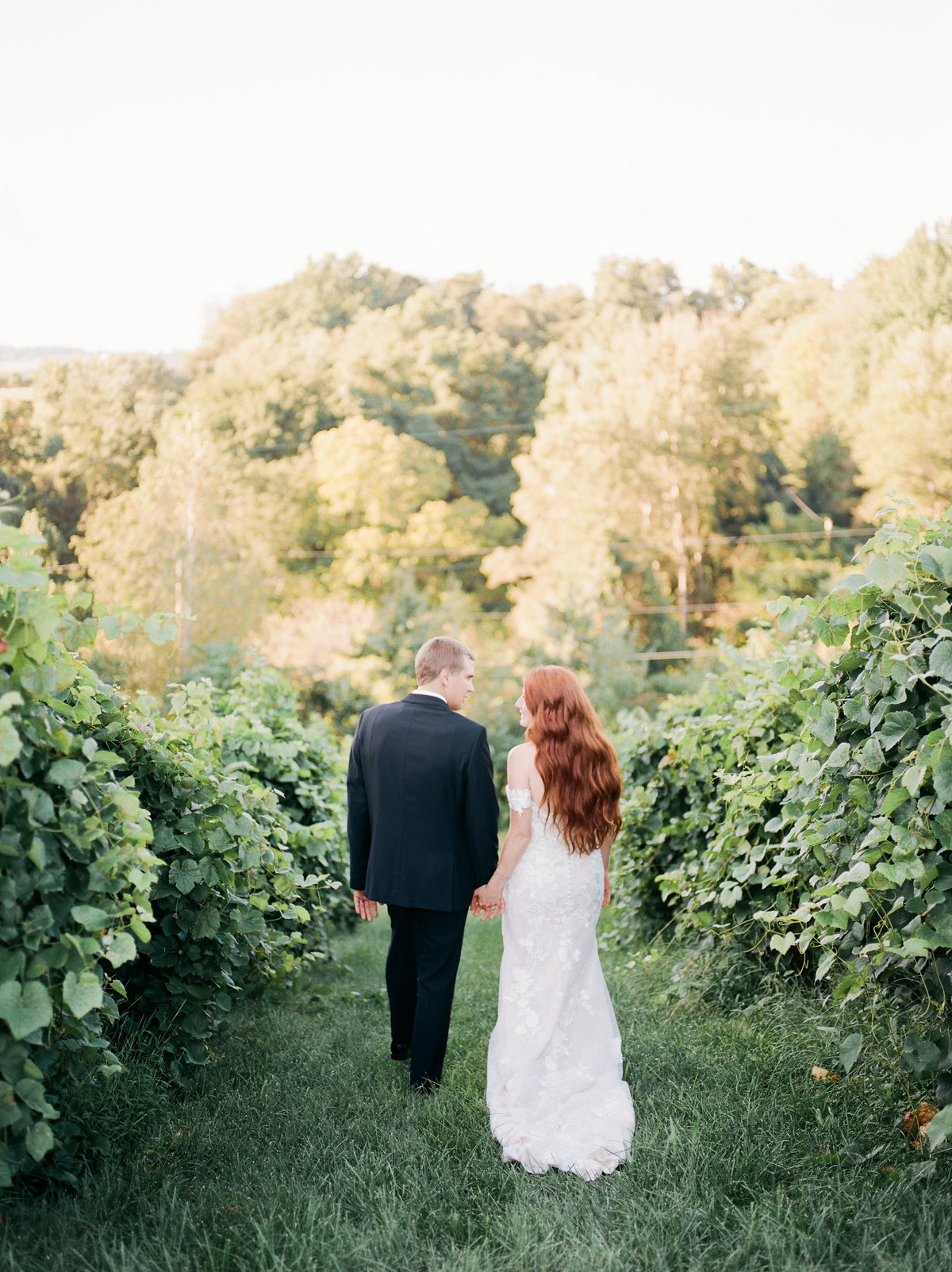 couple wearing wedding attire walking through green grass