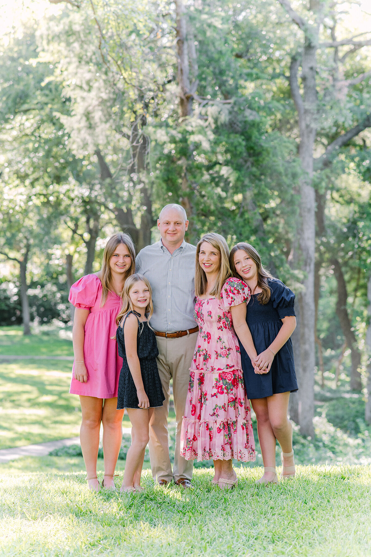 Family of five standing in a park with coordinating pink and navy clothing.