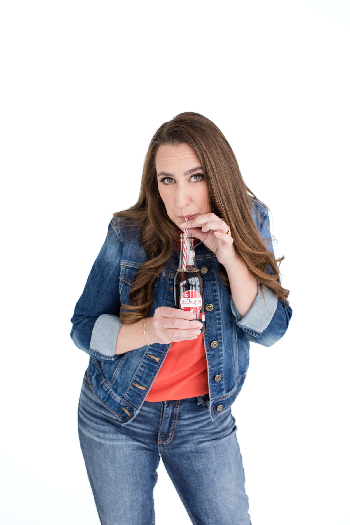 brand photo by brand photographer near me with woman holding a soda bottle and drinking the soda inside while making eye contact with the camera