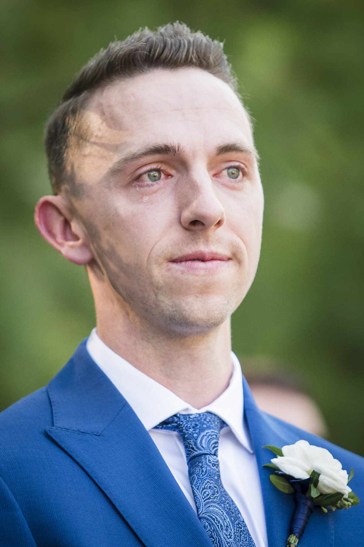 A groom sheds a tear as he watches his bride walk up the aisle.