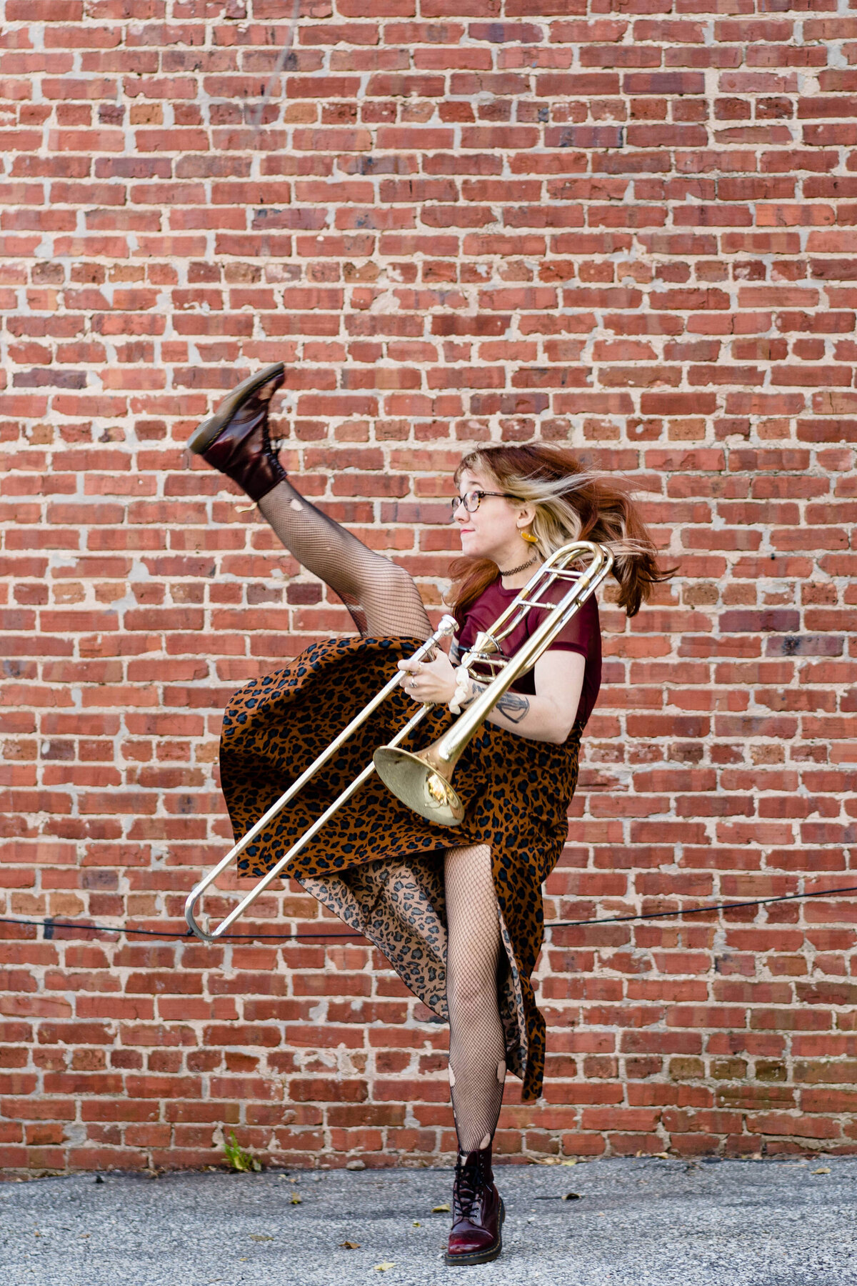 A person holding a trombone while kicking one leg up.