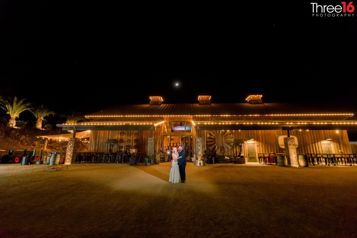 Bride and Groom pose for photos at night with Peltzer Winery behind them