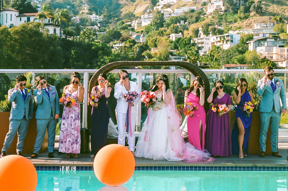 A wedding party standing on the opposite side of a pool.