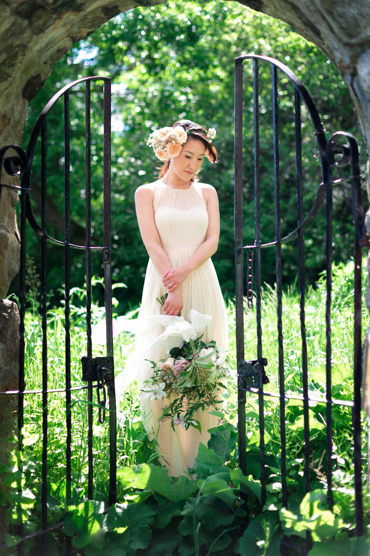 The bride is framed by a stone wall and gate while among the plants on her wedding day at Inn at Castle Hill at Barn at Crane Estate wedding