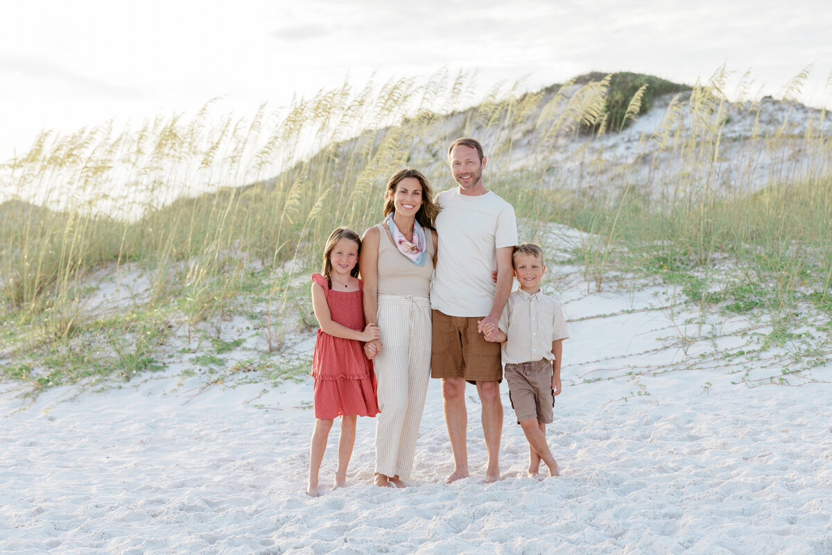 A family of four wearing mostly neutral colors in Watersound Beach with a sand dune behind them.