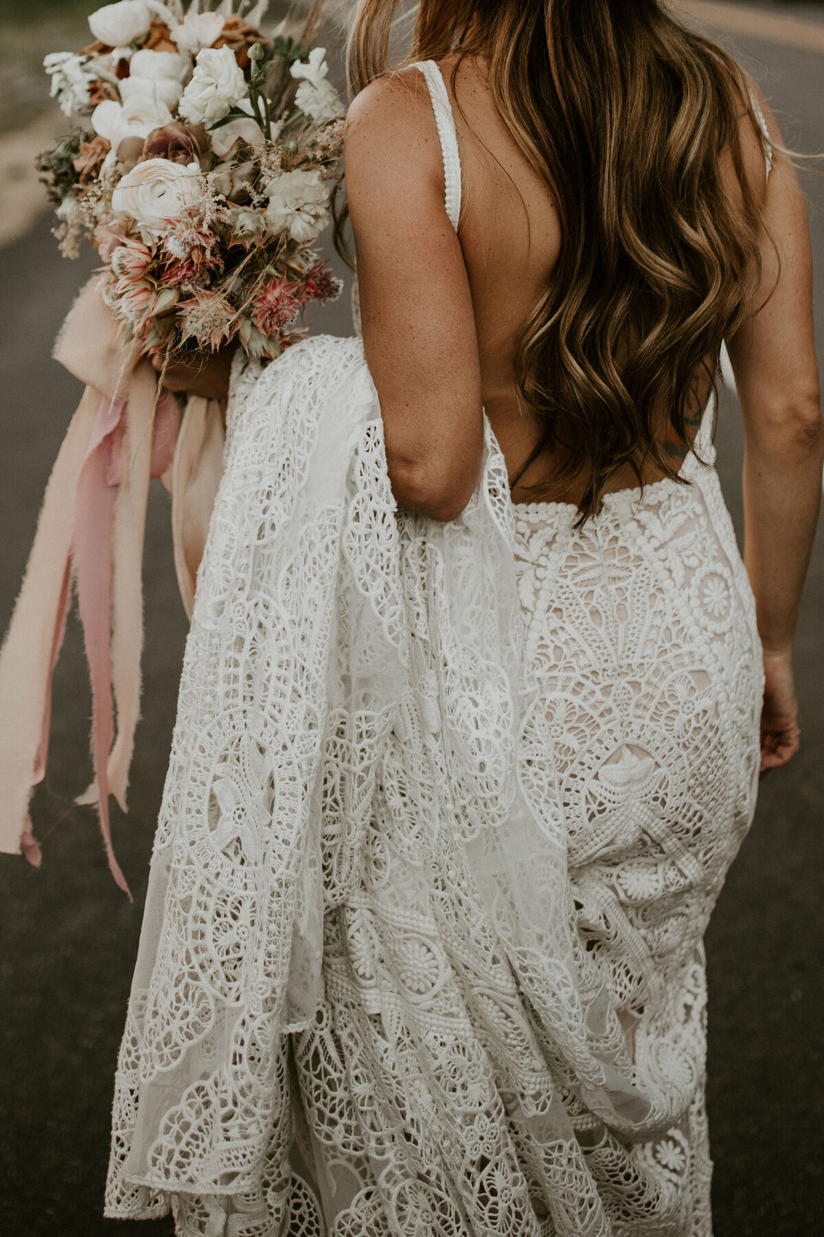 bride wearing a white wedding gown poses while holding her gown and a bouquet on one hand