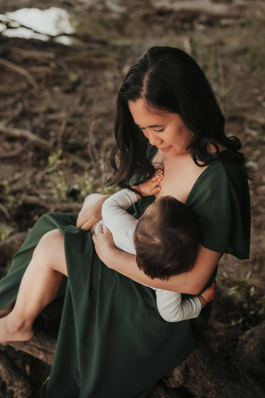 A mom nursing her son wearing a beautiful long green dress