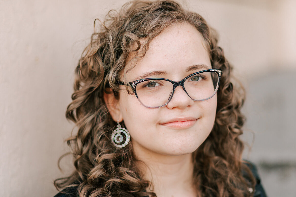 A teenager with brown curly hair and black-rimmend glasses smiles