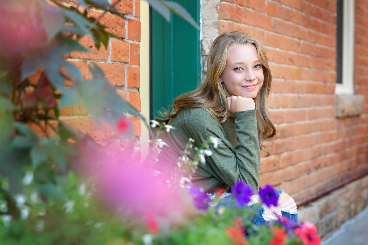 A senior girl smiles over a pot of flowers in an urban alley