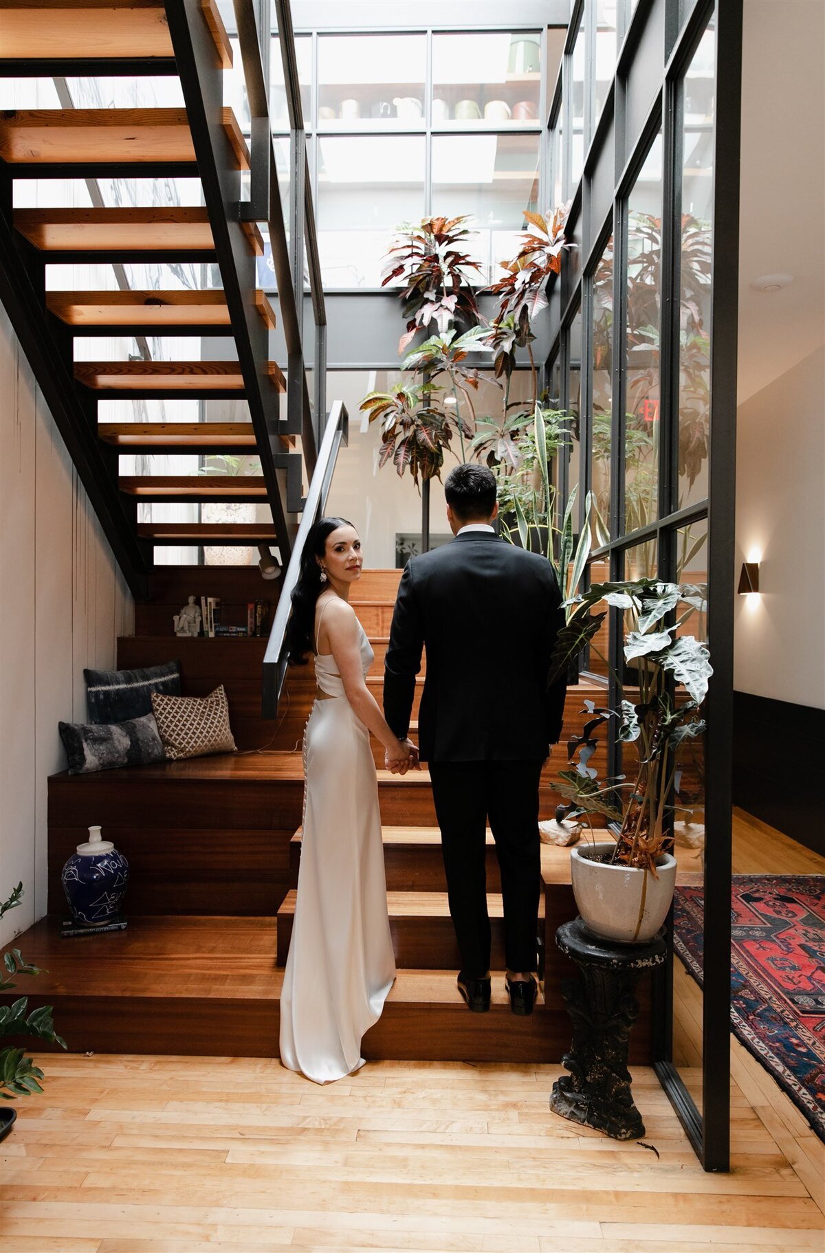 Newlyweds hold hands on modern staircase at a Brewery wedding as bride looks over her shoulder toward the camera.