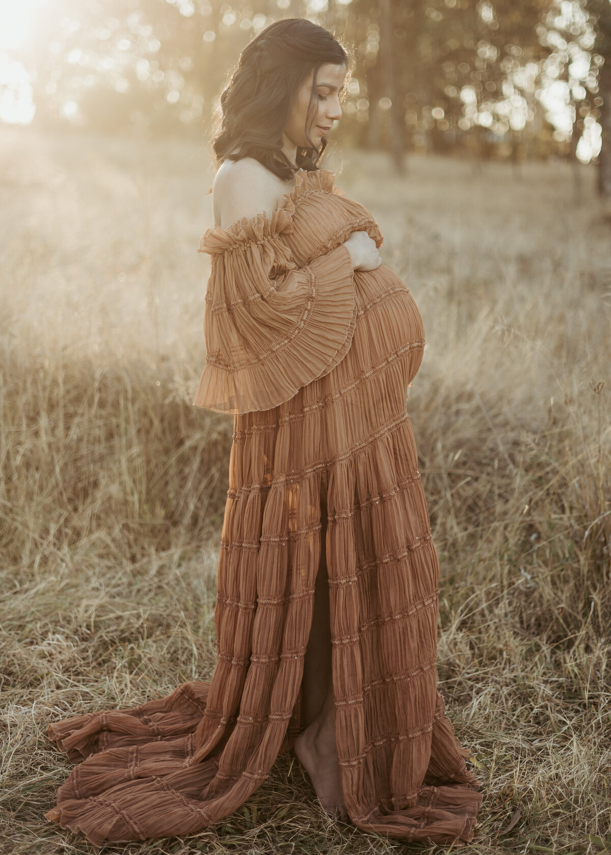 Gorgeous Sydney mama wearing a long brown strapless dress while gazing lovingly at her growing belly growing a baby for her maternity photoshoot.