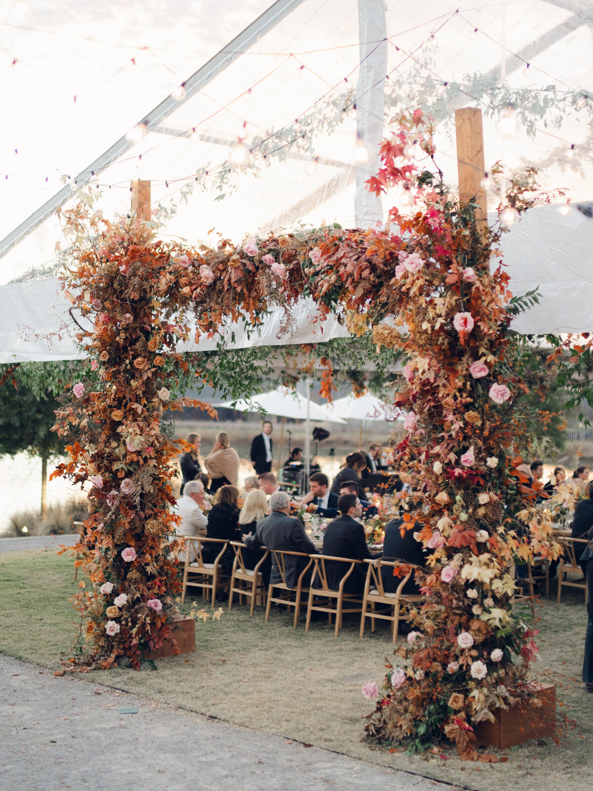 Tent entrance installation for fall wedding at Southall Farm & Inn. Lush floral install makes large impact in blush, tangerine, caramel, and mustard yellow flower colors. Large fall branches and roses make a statement for this wedding reception tent entrance. Destination floral design wedding outside Nashville, TN. Design by Rosemary & Finch Floral Design in Nashville, TN.