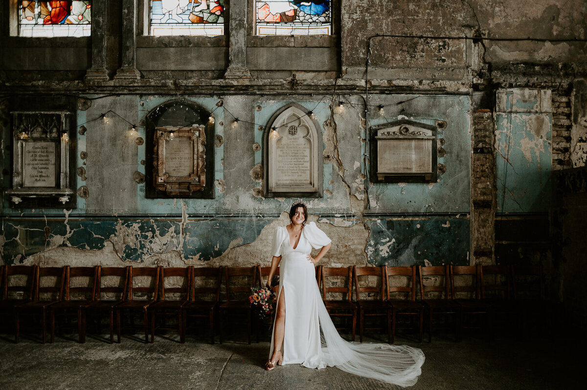 A bride stands with her hand on her hip holding a pink bouquet at The Asylum Chapel in London.