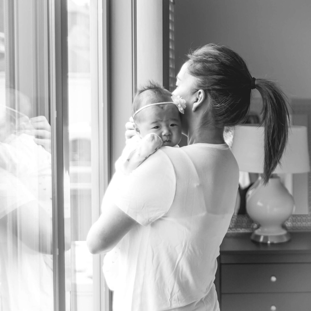 black and white photo of mom at the glass door holding baby and soothing her