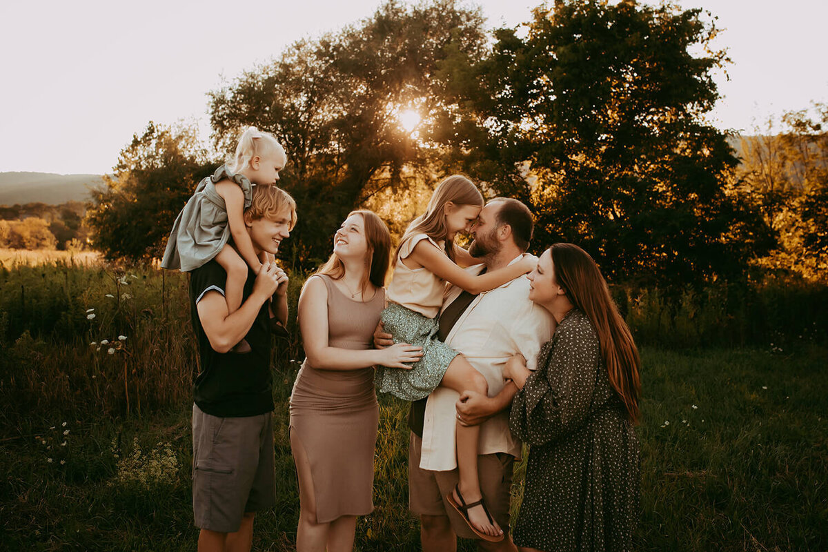 a family of 6 hugging and interacting in a field at sunset