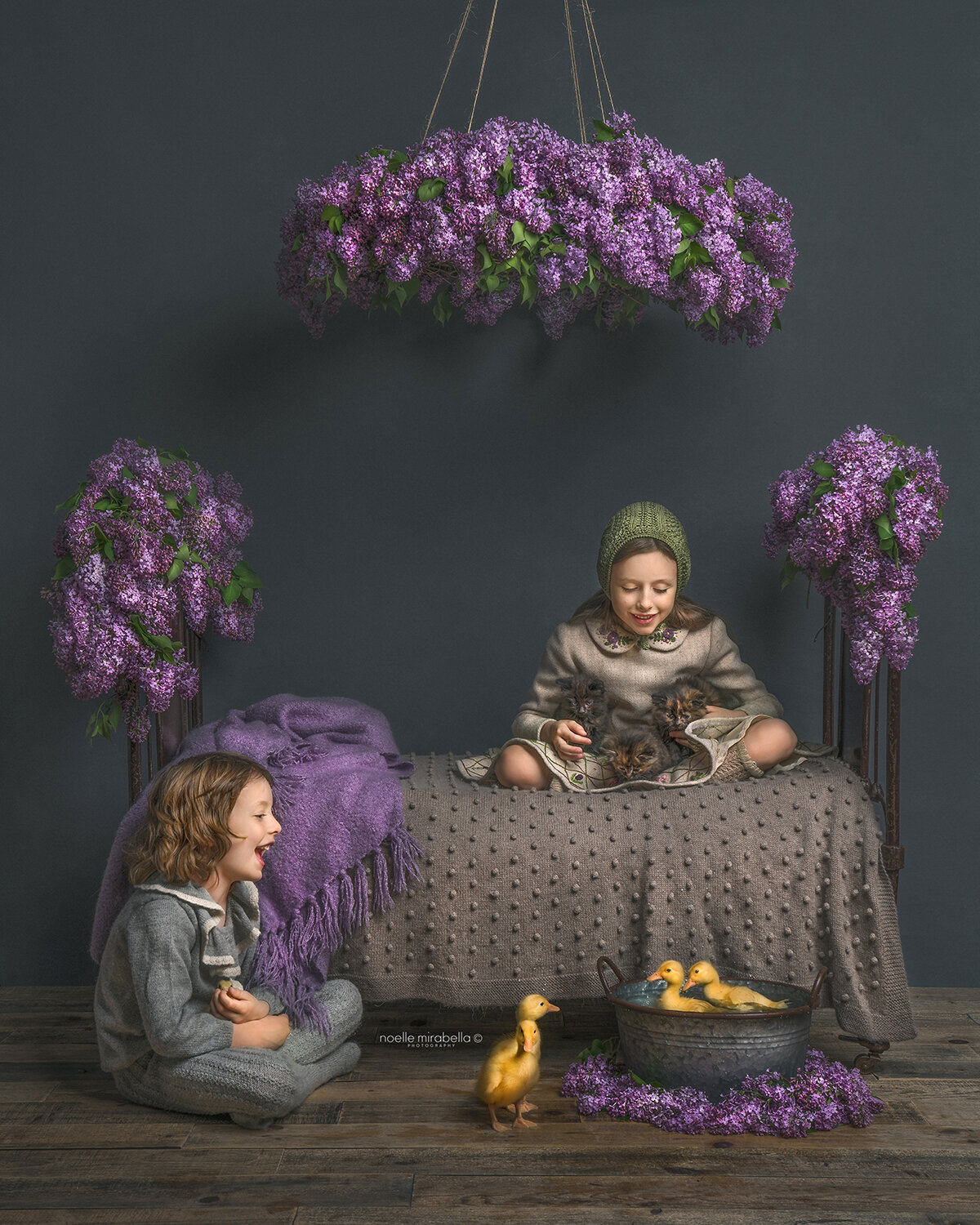 Children playing with baby duckklings on bed covered in fresh lilac blooms.