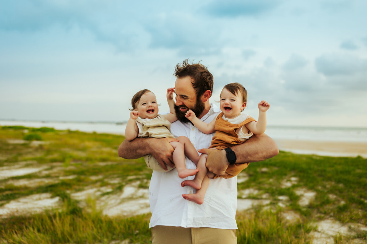a father holding his twin boys laughing at the beach