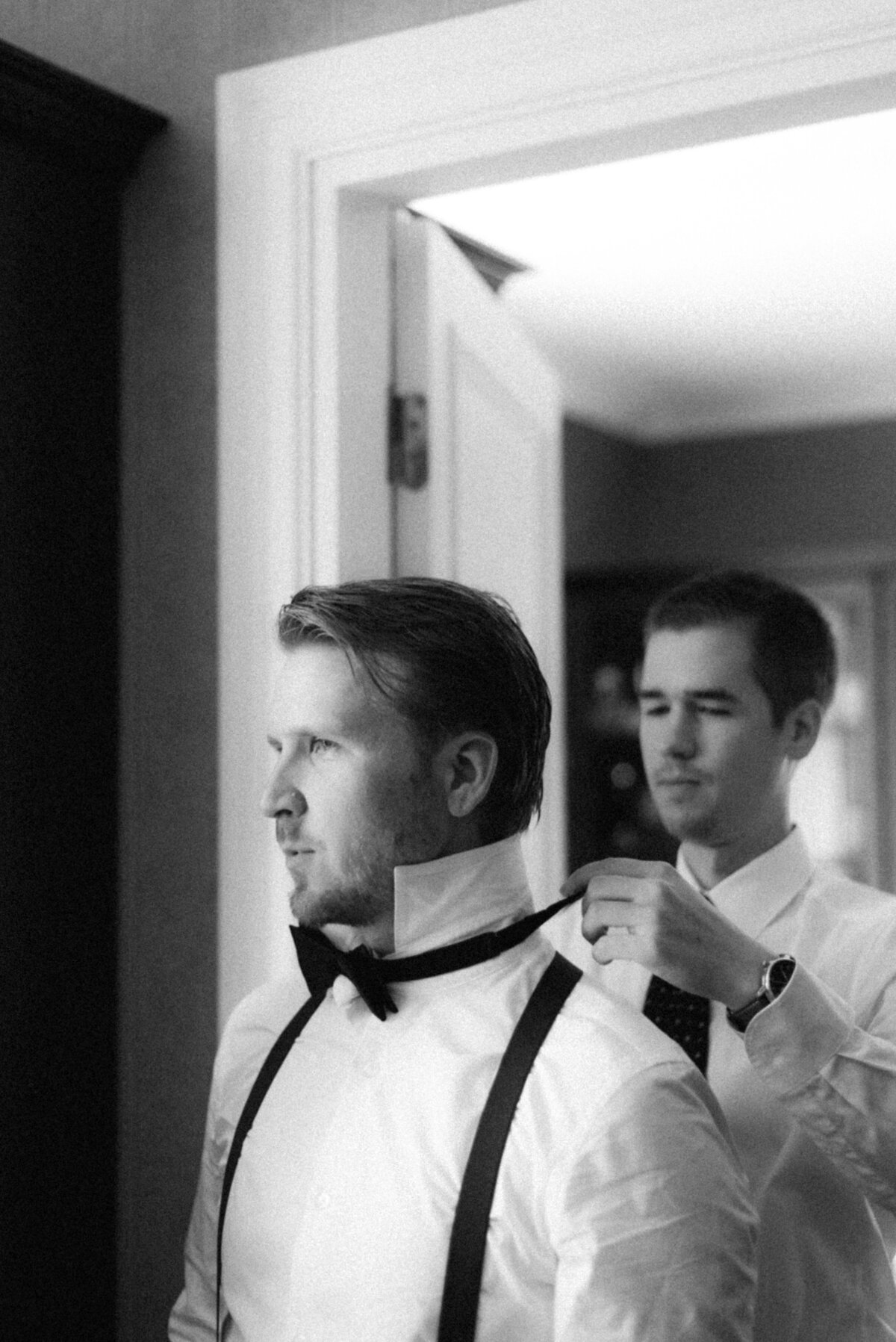 The bestman is helping the groom to put on the bowtie in an image captured by wedding photographer Hannika Gabrielsson.