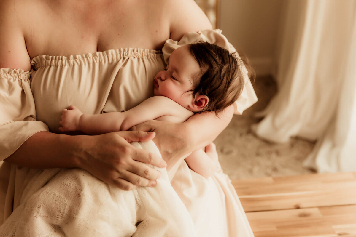 Sleeping baby girl with beautiful dark brown hair in her mother's arms.