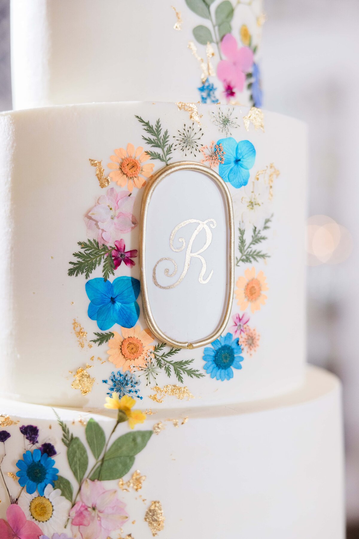 Close-up of a multi-tiered white wedding cake adorned with colorful edible flowers and a gold-framed oval plaque with "Park Farm Winery" on the middle tier.