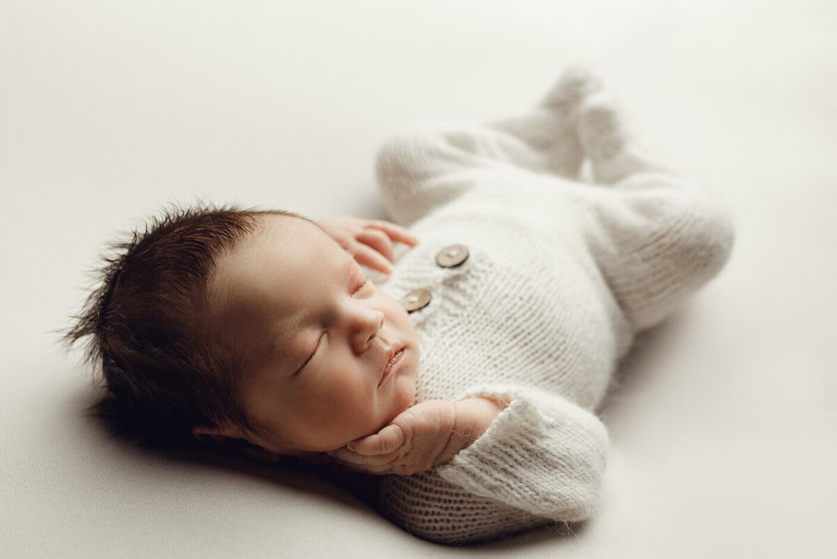 newborn boy sleeping on his back with his hand under his chin