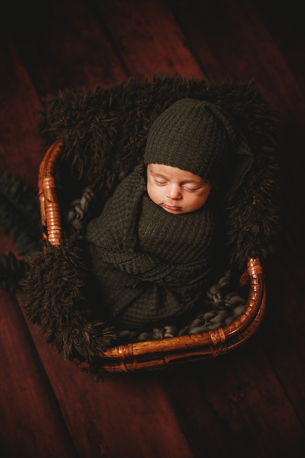 Family photographers Maryland captures newborn photography with baby in a dark grey swaddle sleeping in a cherry red basket