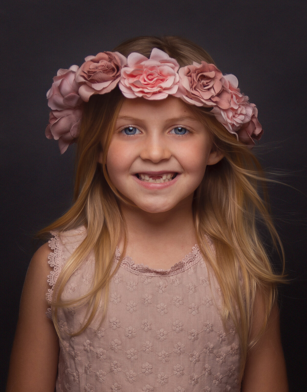 girl child with empty front teeth smiling widely with a crown of pale peach roses