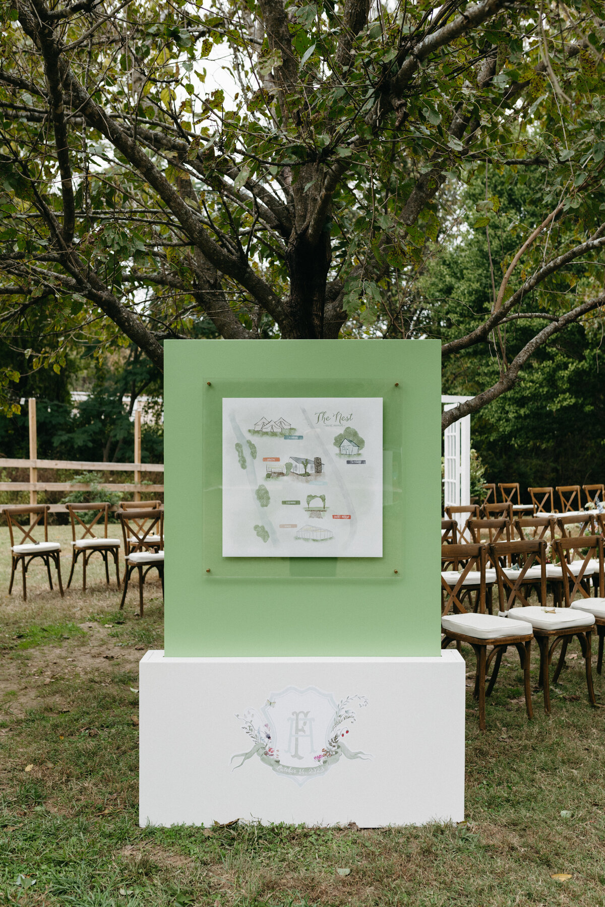 Custom illustrated venue map displayed on a green welcome sign at The Nest in Northwest Arkansas, surrounded by ceremony seating and whimsical outdoor wedding décor.