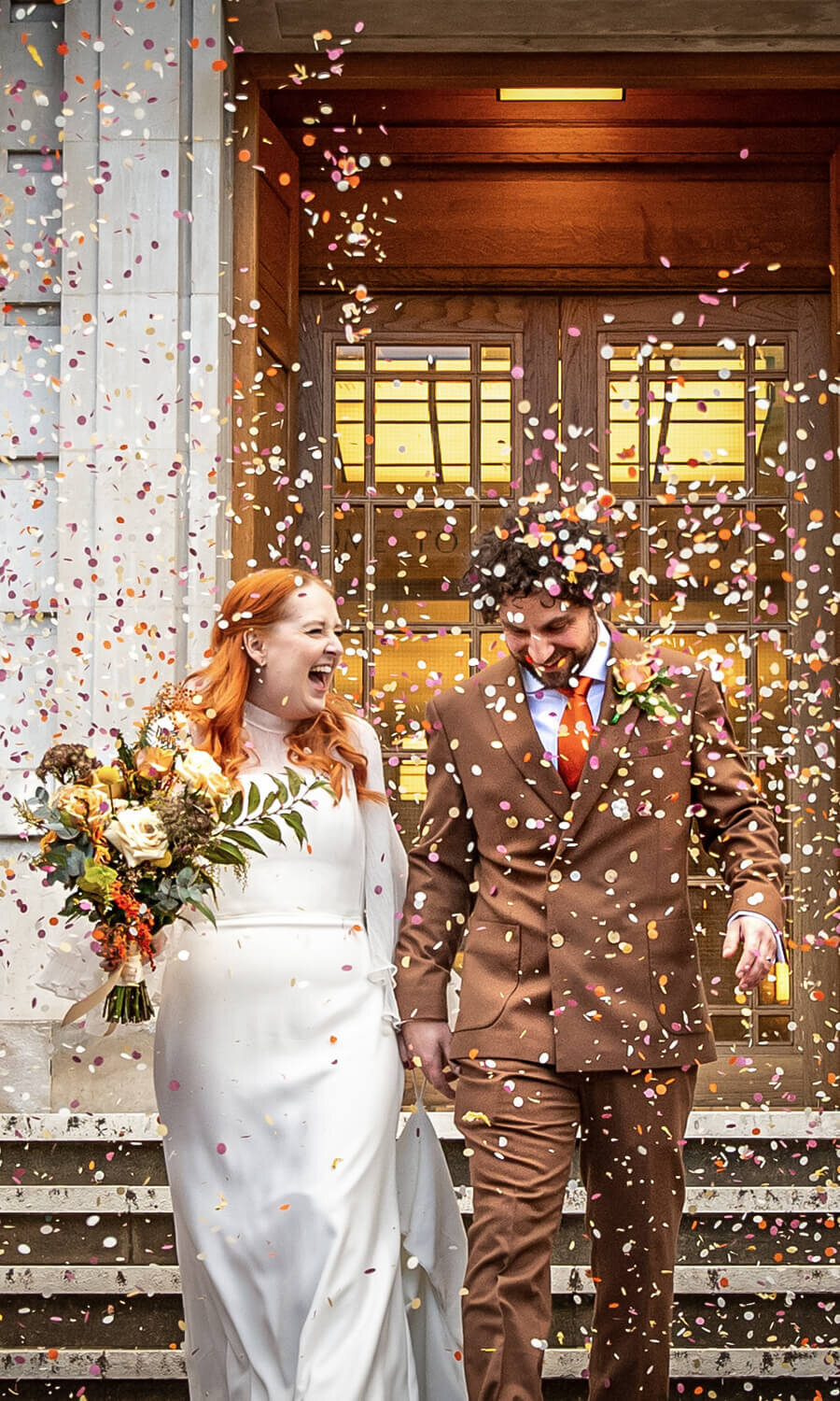 Red head bride and smiling groom walk down stairs outside Hackney Town Hall
