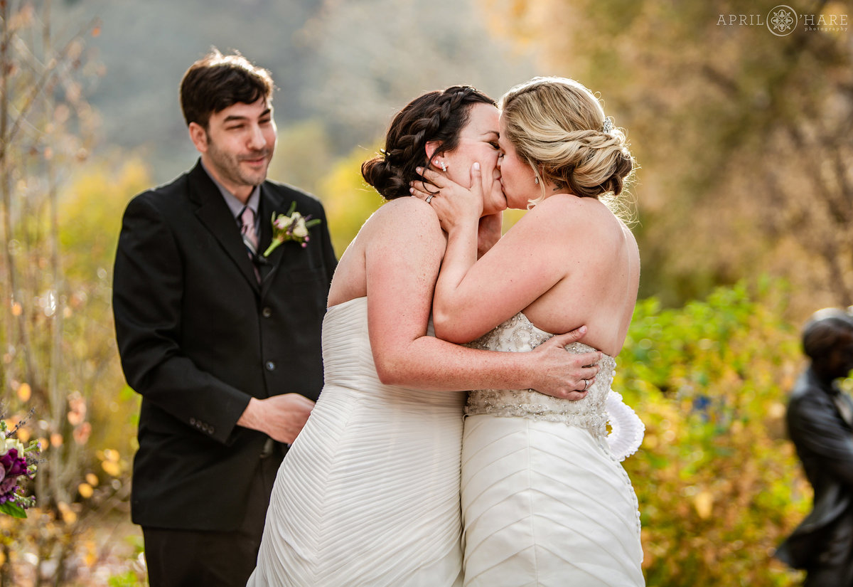 Two brides kiss at their outdoor Golden Hotel Wedding at a same sex wedding ceremony in Colorado during autumn
