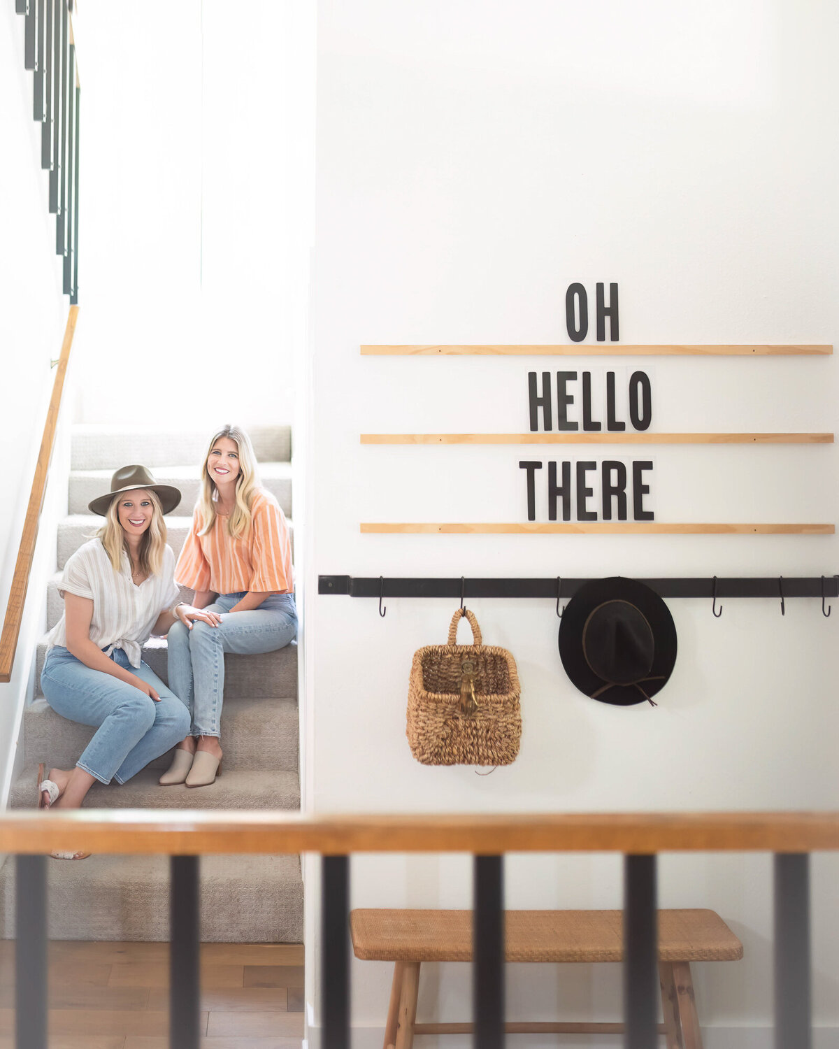 Interior designer sisters sitting on steps, sign on the wall says oh hello there!