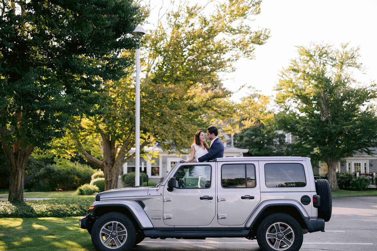 The bride and the groom are standing out of a car's sunroof at Cape Cod, Osterville, MA.