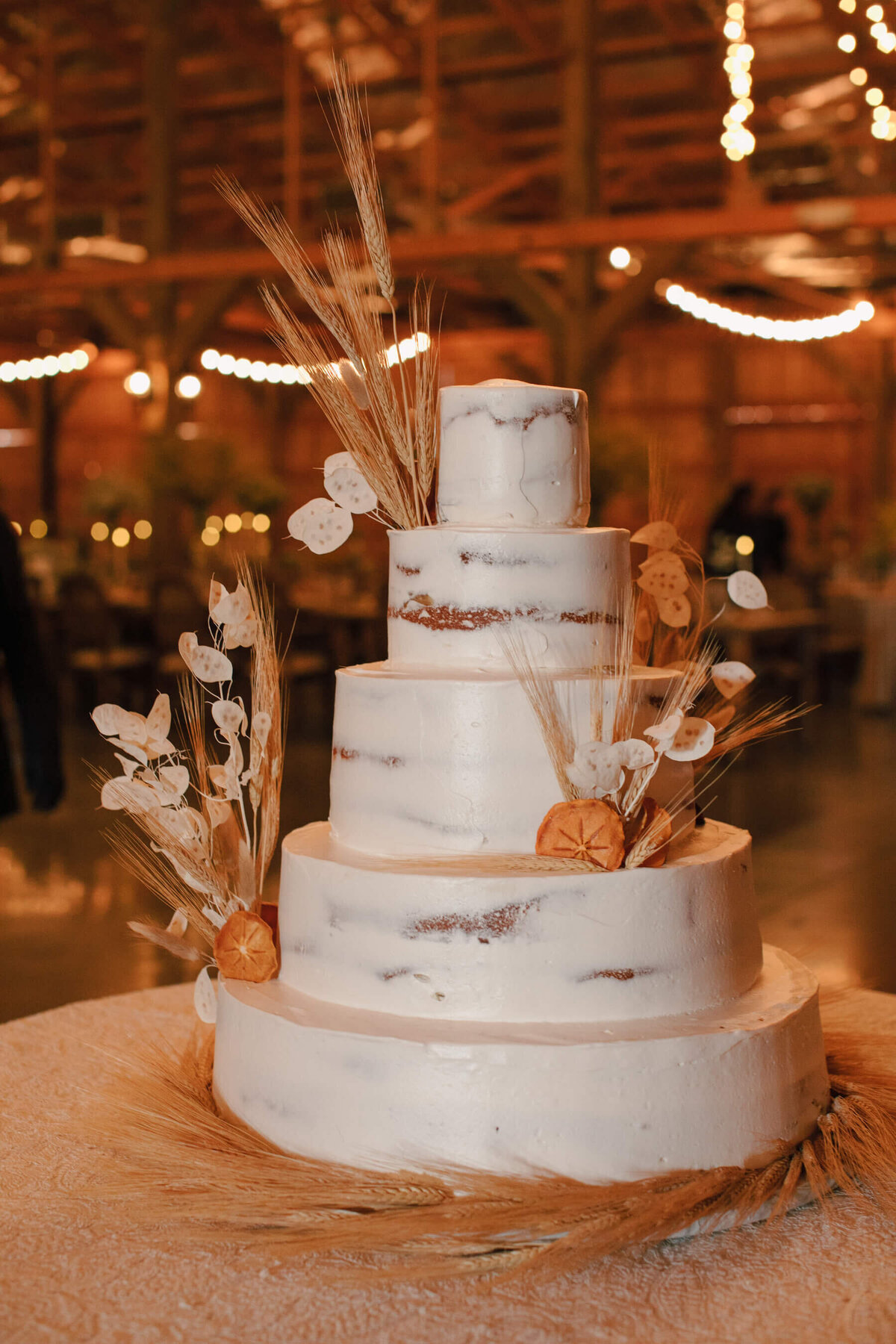 White wedding cake with dried wheat, dried oranges and lunaria.