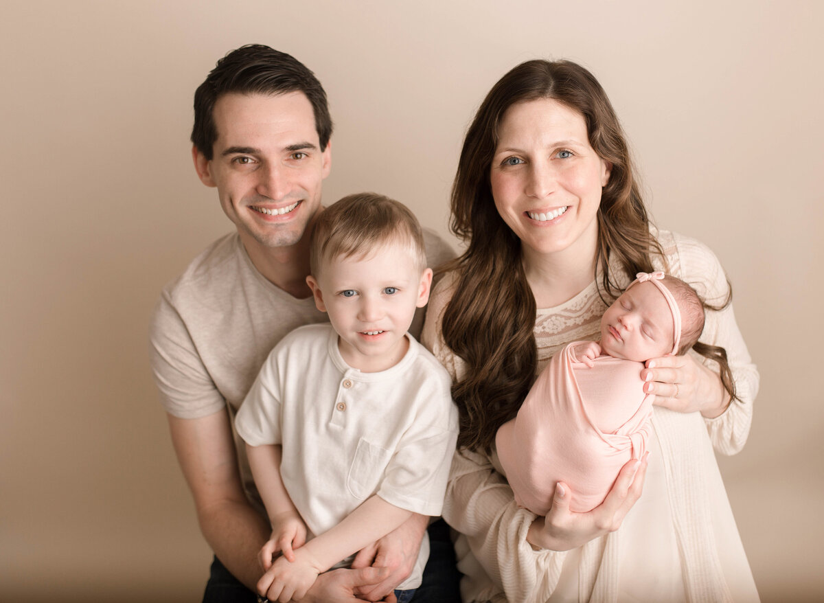 Family in studio smiling at the camera with toddler an dnewborn
