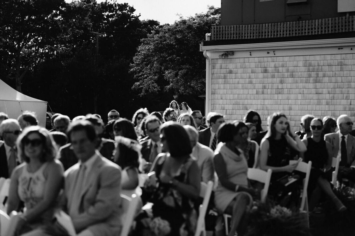 Black and white photo of seated wedding guests waiting for the bride, in an outdoor wedding at Wianno, Cape Cod, MA.