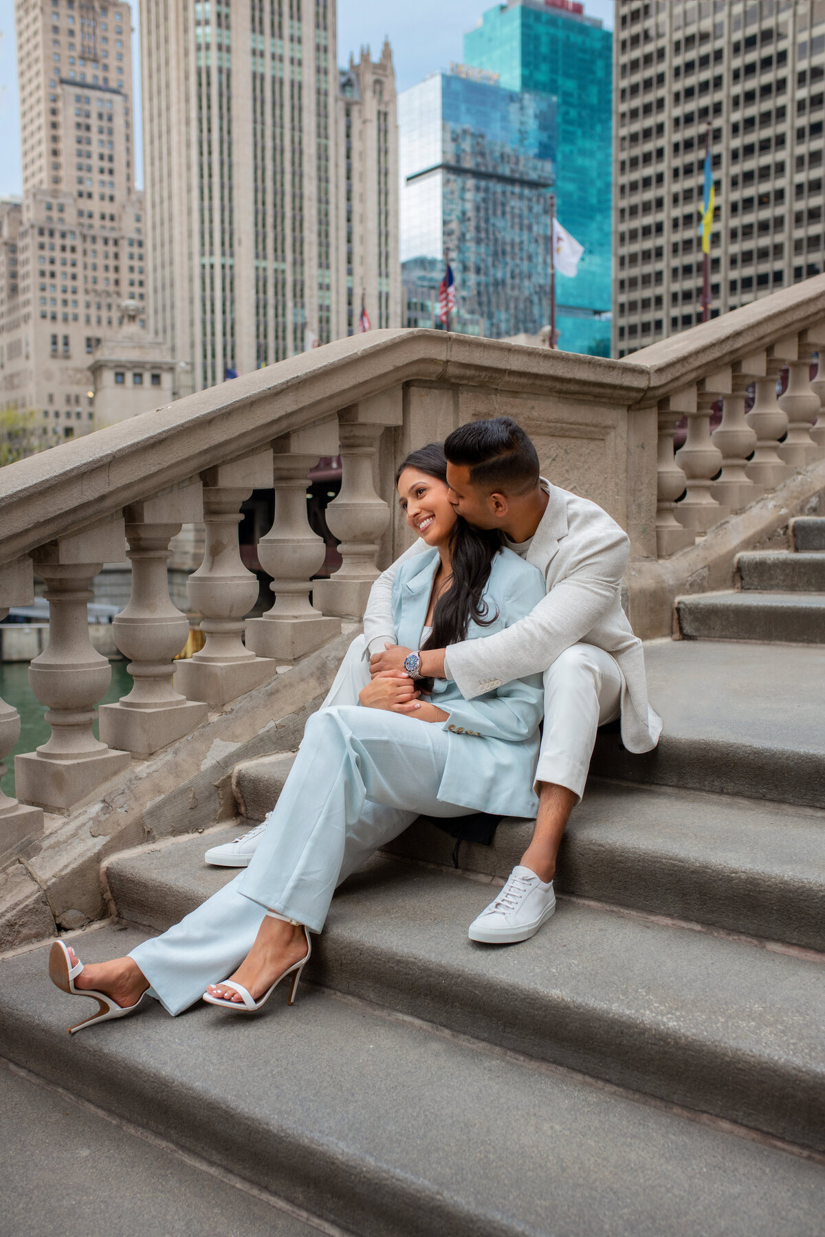 Engaged Indian couple in  business suites sitting on Chicago riverwalk stairs and holding each other