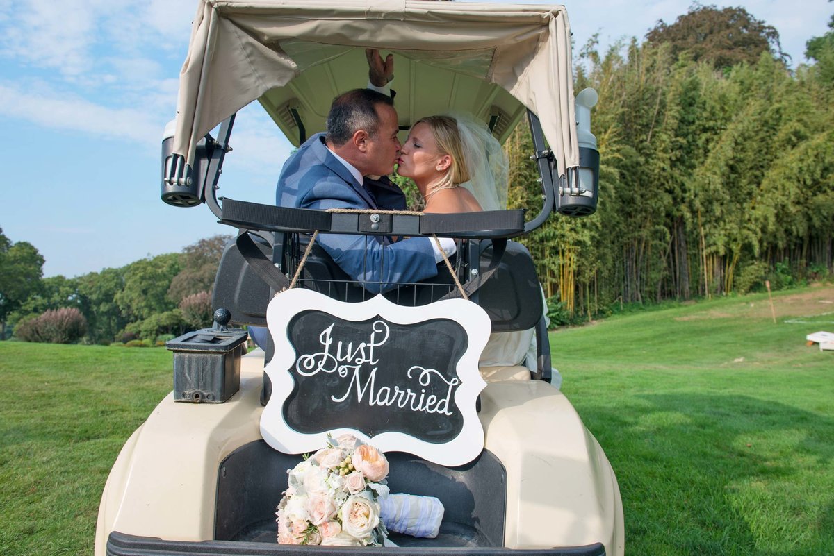 Bride and groom kissing on just married golf cart at Huntington Crescent Club