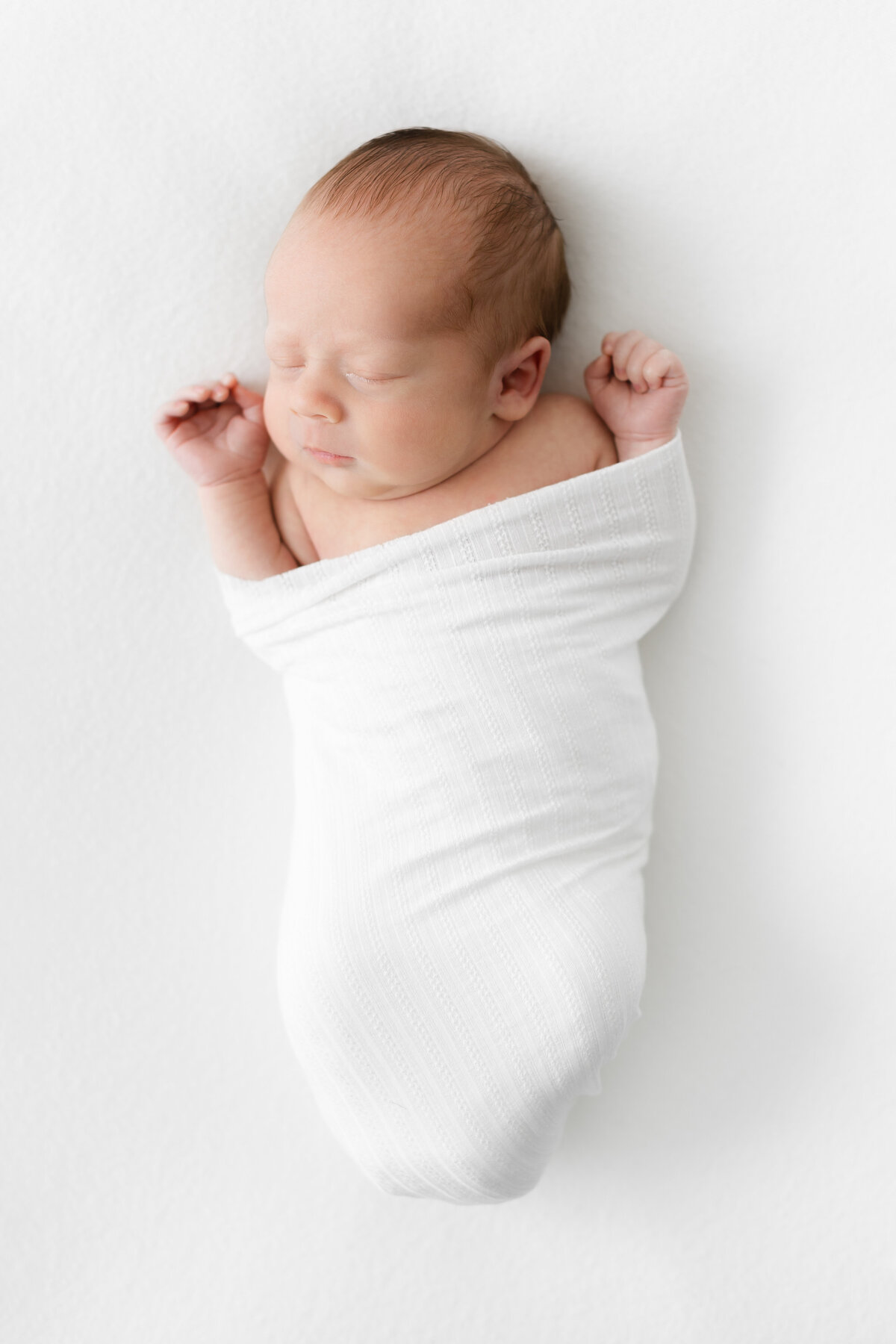 A baby boy swaddled with his arms out in a white blanket at a Northern Virginia Newborn Photography session
