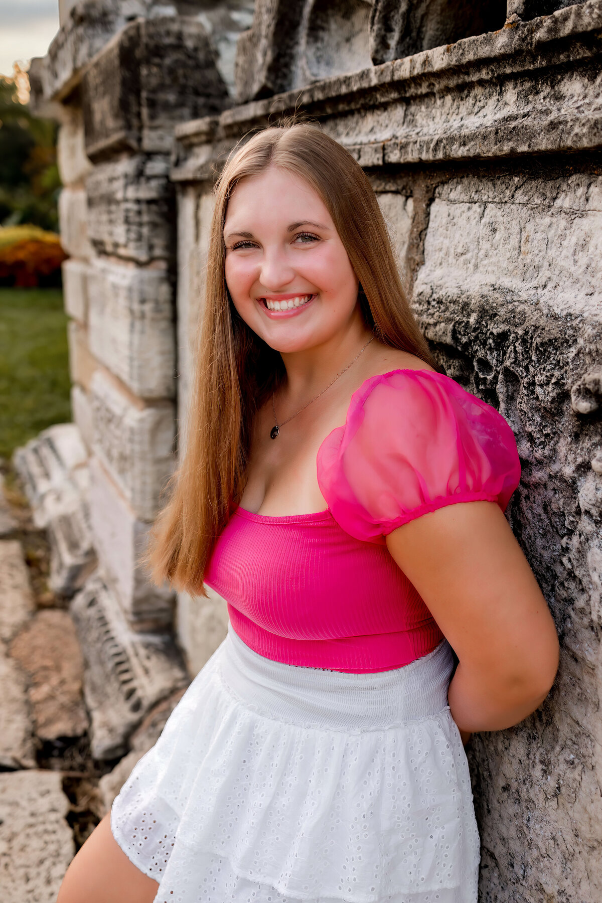 A pretty girl is posing for her senior portraits in twoer grove park next to the ruins.