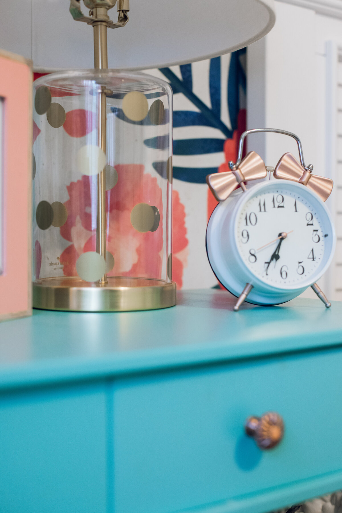 a gold lamp and vintage alarm clock on a blue night table
