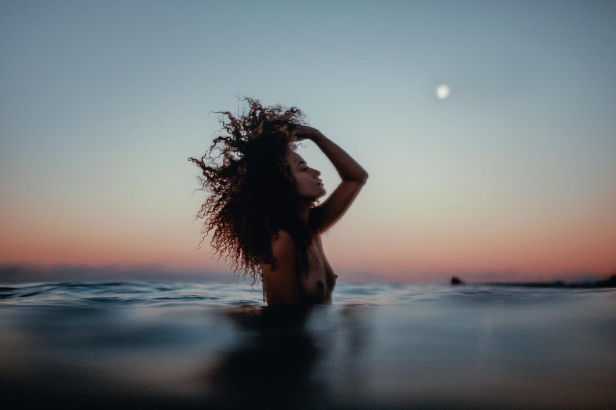 Woman throws her hair back in the moonlight during her Maui boudoir photoshoot